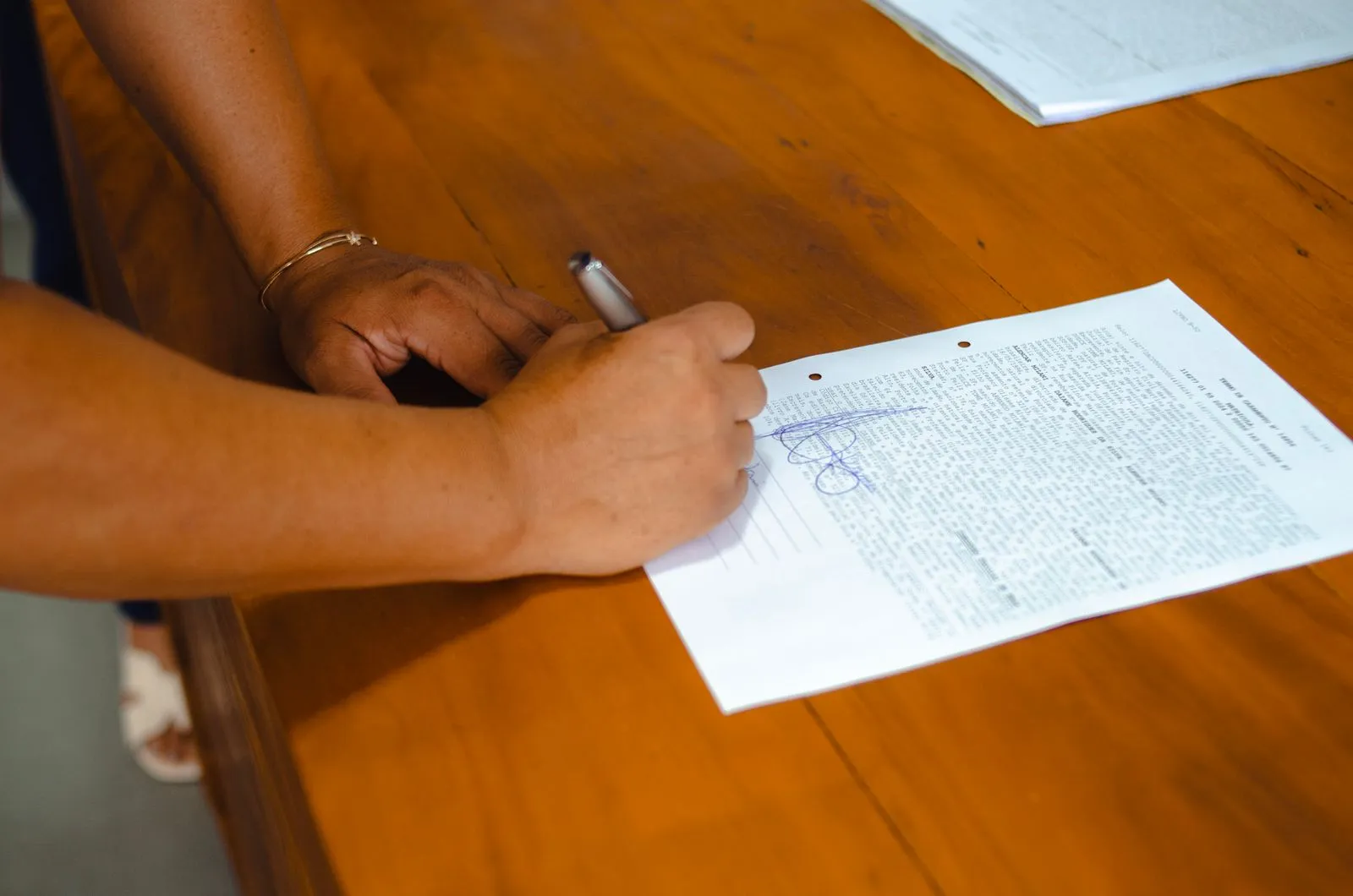Une personne prépare une lettre de résiliation, contrat et stylo posés sur un bureau clair.
